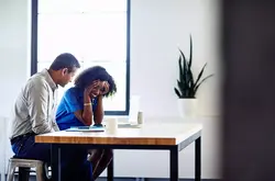 Smiling male and female sitting at a table. Both looking down at the table.