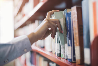 A person pulling a book from a shelf