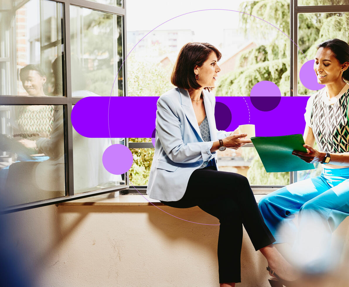 Two female sitting on a window sill looking at papers.