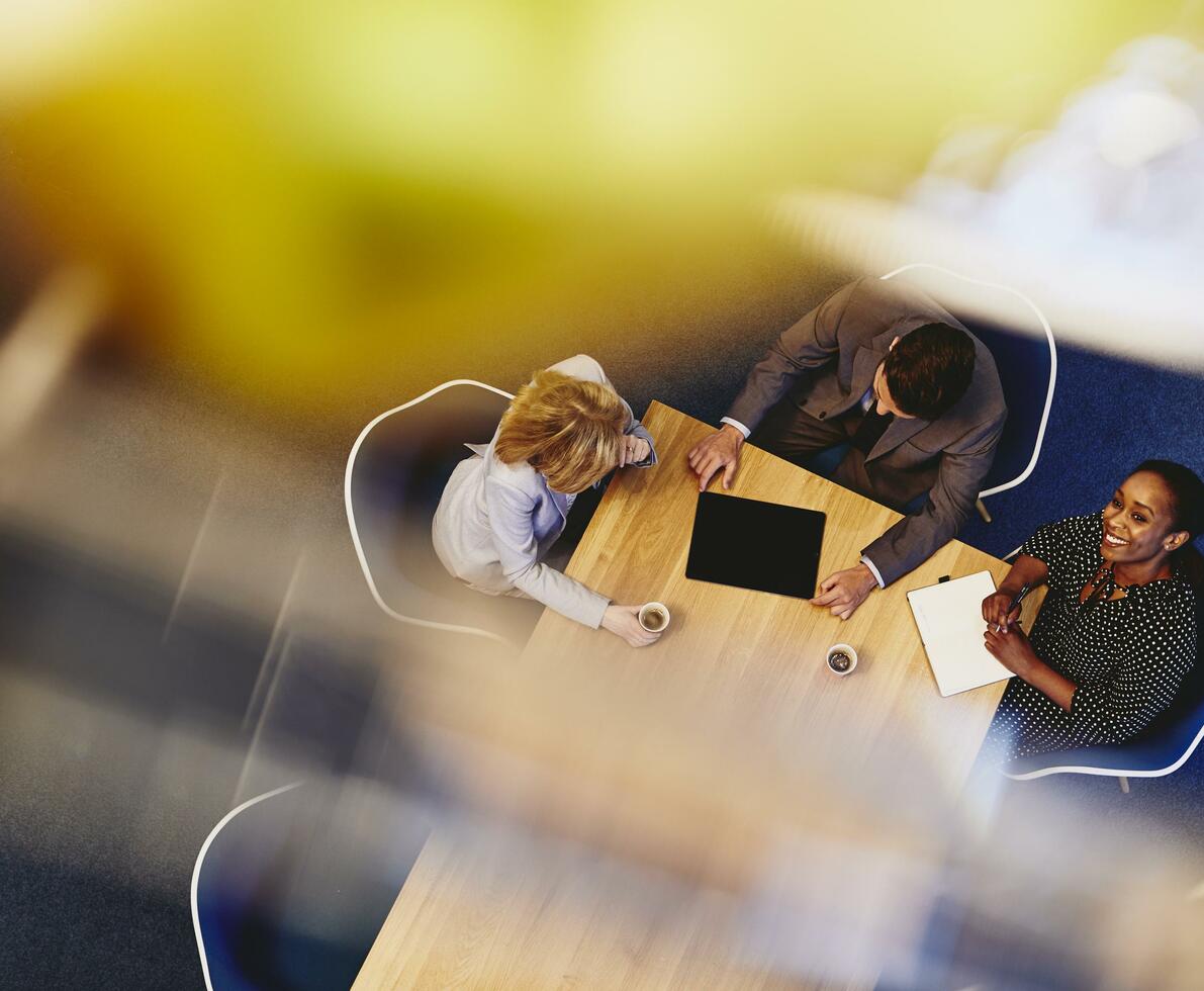 People having a meeting in an office. Woman looking up & smiling. Primary color: yellow.