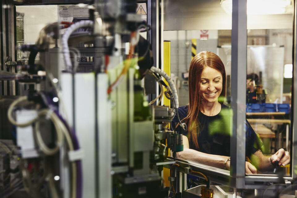 Smiling female operating a machine on a production site. 
