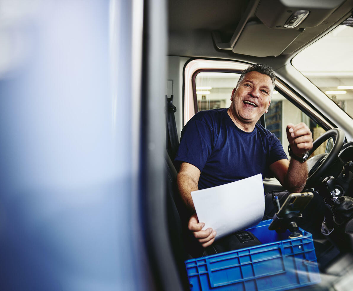 Smiling male sitting in driver's seat of a logistics truck holding a piece of paper
